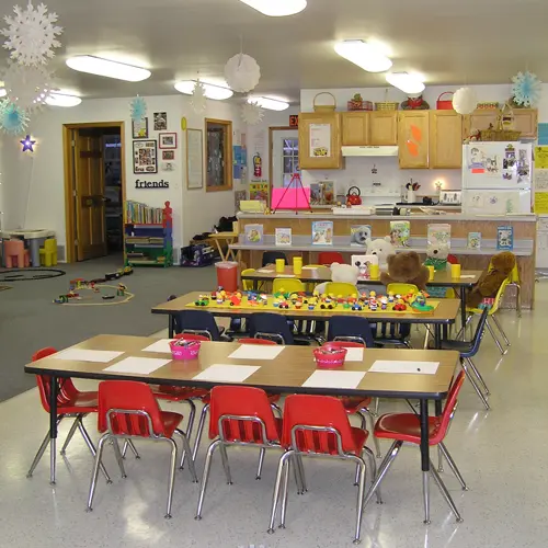 A view of a preschool classroom with small tables and chairs arranged for activities.