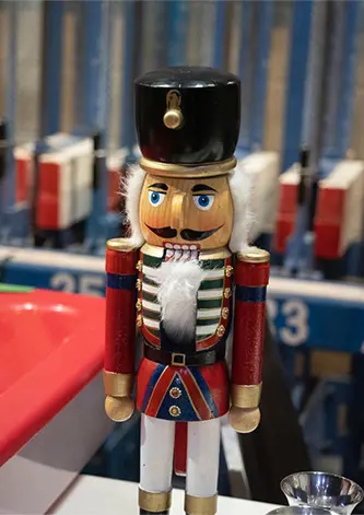 A wooden nutcracker figure stands in front of a blue industrial rack.