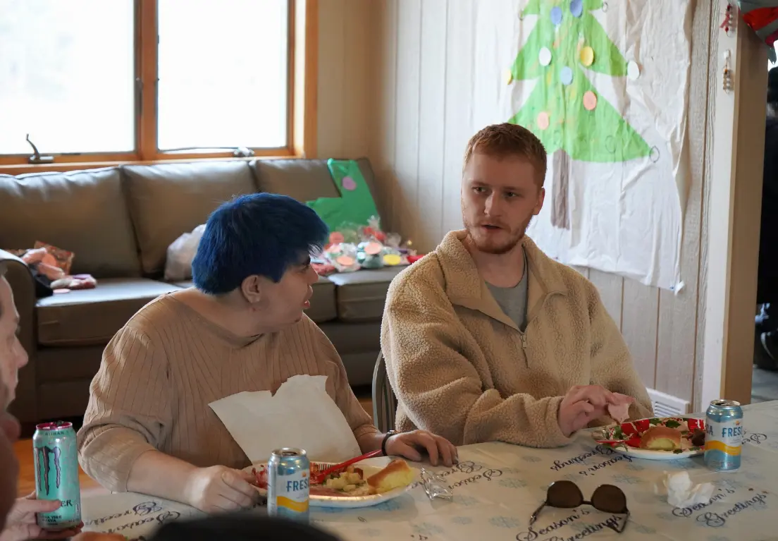 Two people sit at a table decorated with a Christmas-themed tablecloth.