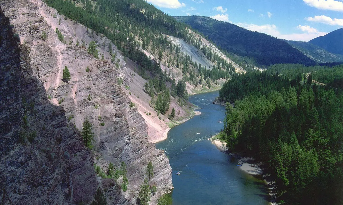 A river flows through a deep canyon surrounded by mountains and pine forests.