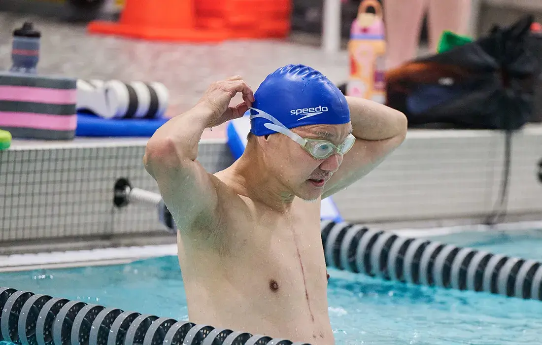 A man adjusts his swim cap while standing in a swimming pool.