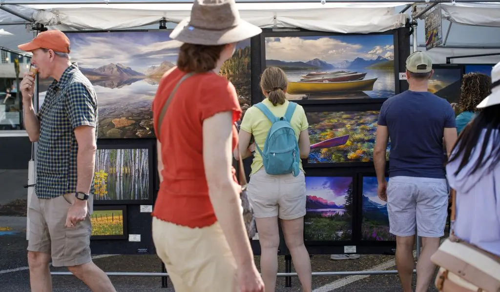 People browse through an outdoor art display featuring landscape photography.