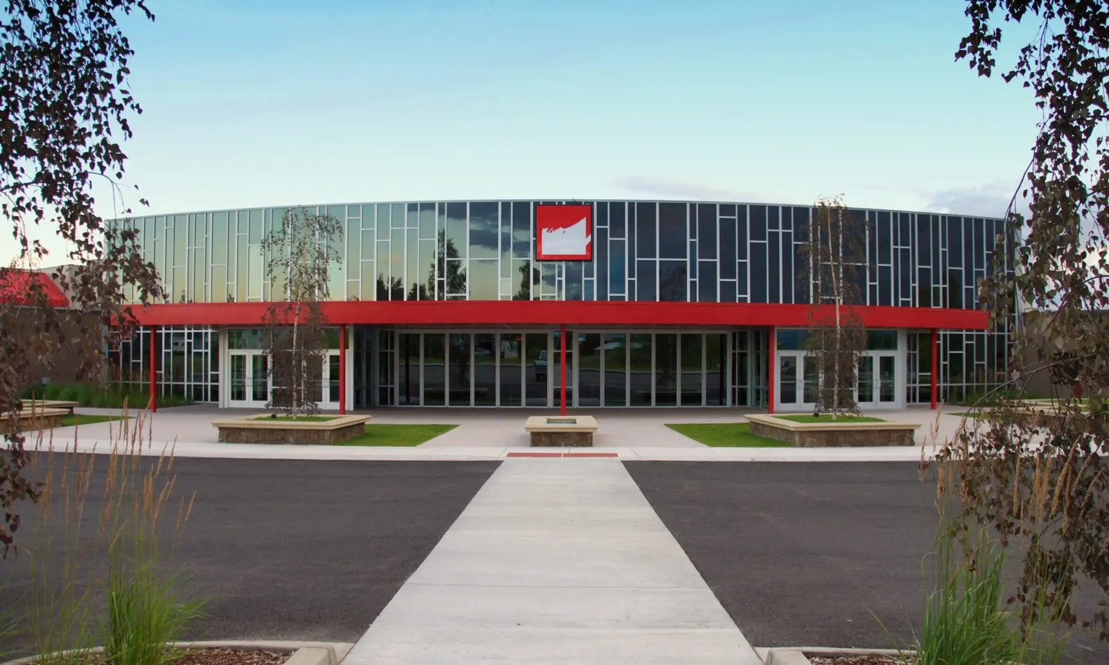 A modern building with a circular glass facade and a prominent red structure across the front entrance.