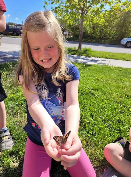 A young girl holds a butterfly in her cupped hands outdoors.