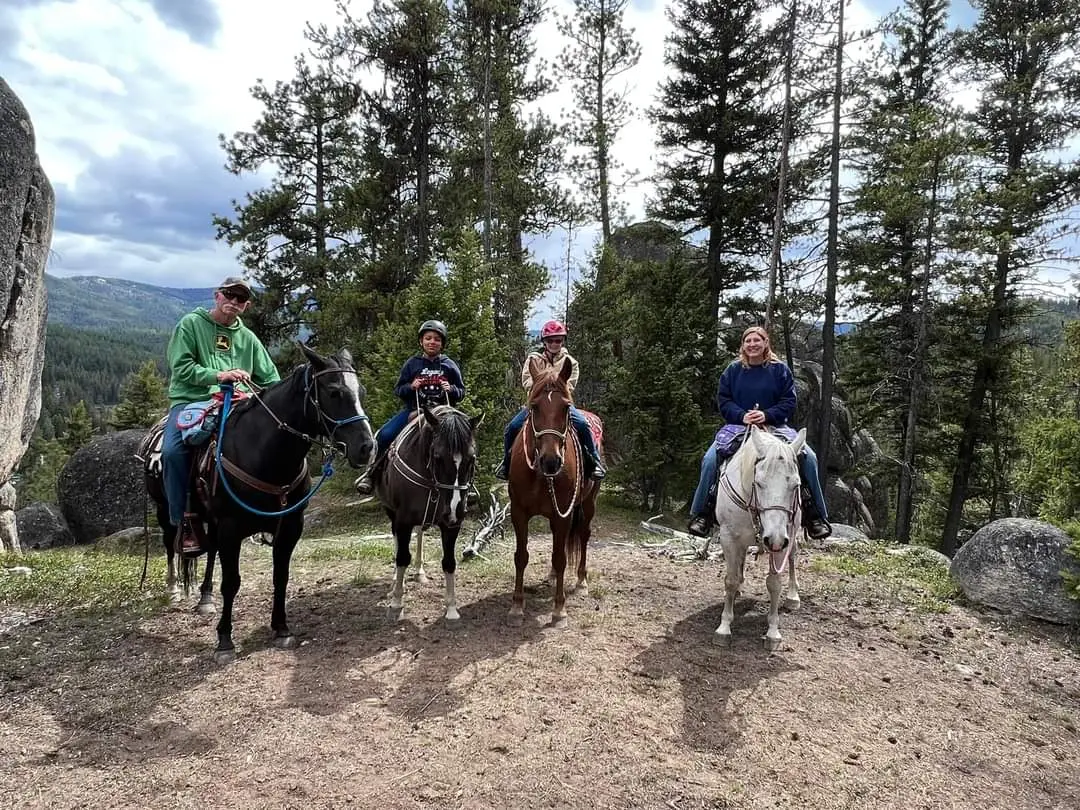 A family rides horses on a wooded trail.