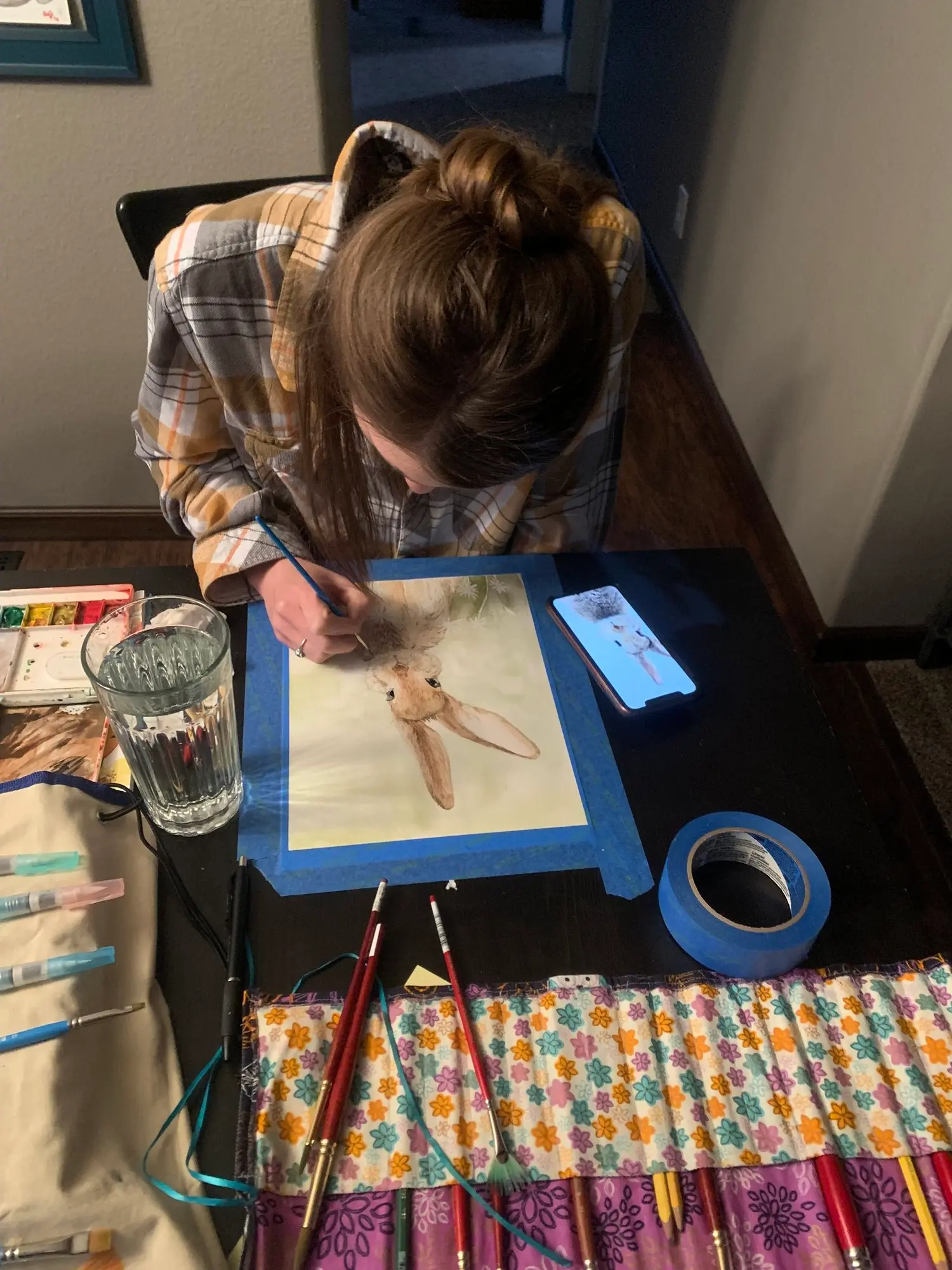A person paints a watercolor picture of a rabbit while referencing an image on a smartphone.