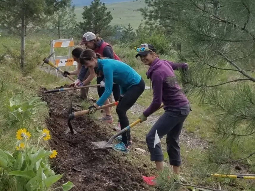 A group of women work together on a trail construction project outdoors.
