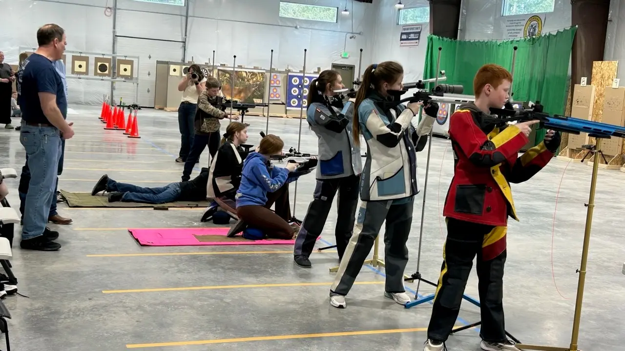 A group of students practices marksmanship with rifles at an indoor shooting range.