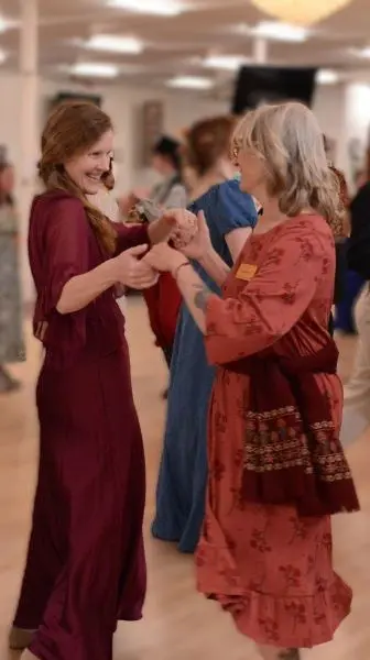 Two women smile as they dance together indoors.