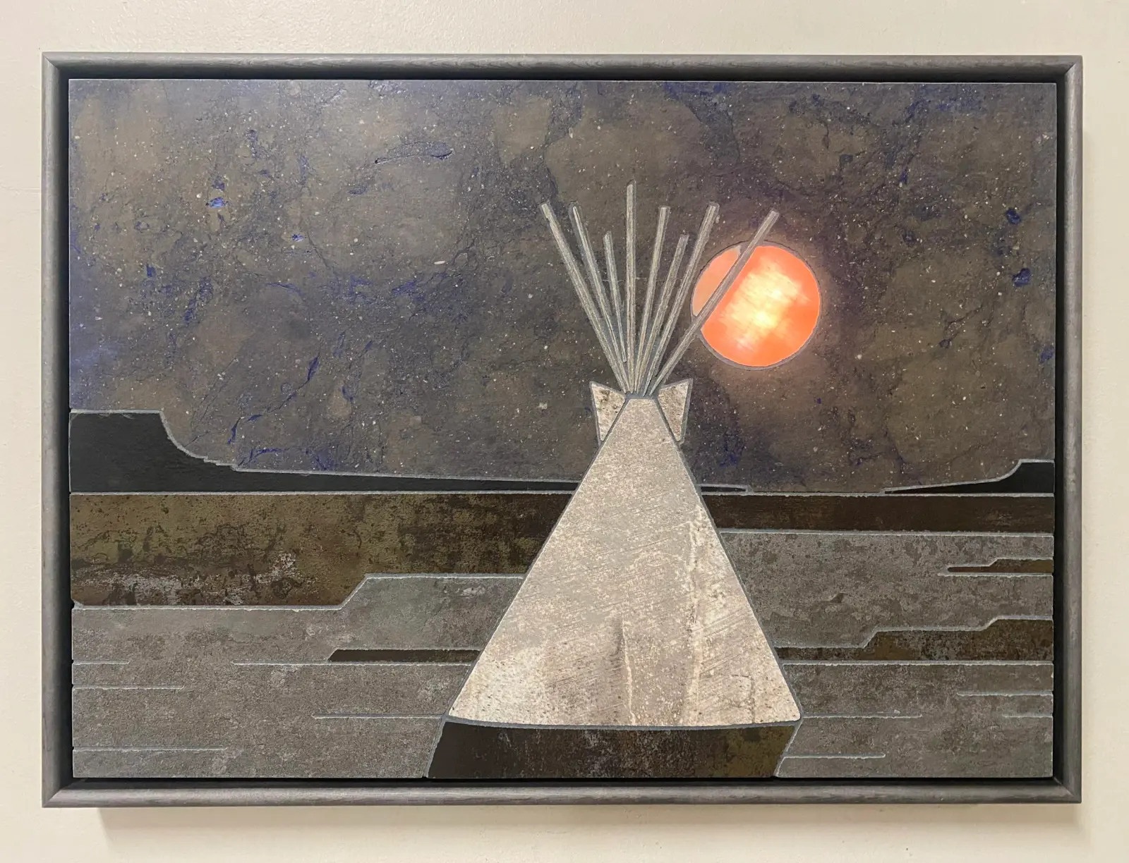 A framed piece of artwork depicts a teepee standing in a landscape beneath a luminous orange moon.