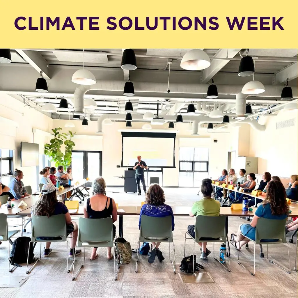 A speaker addresses an audience seated at tables in a room during a climate solutions event.