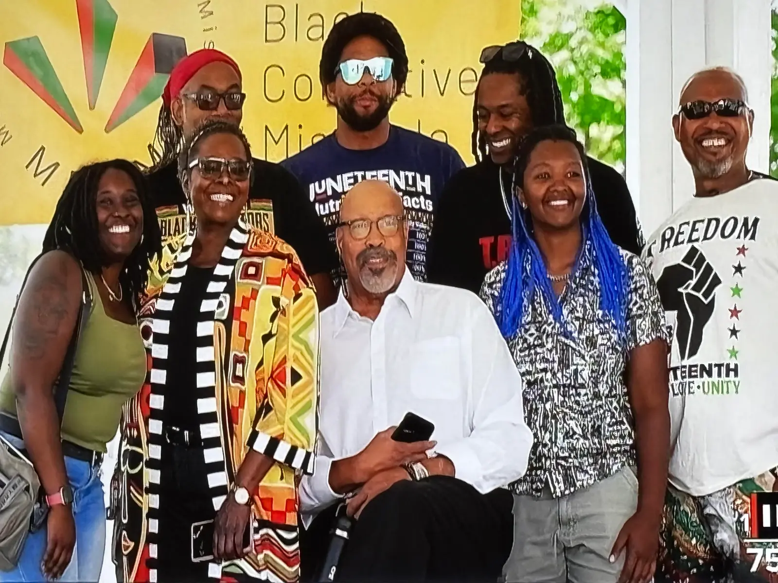 A diverse group of adults stands together in front of a yellow banner.