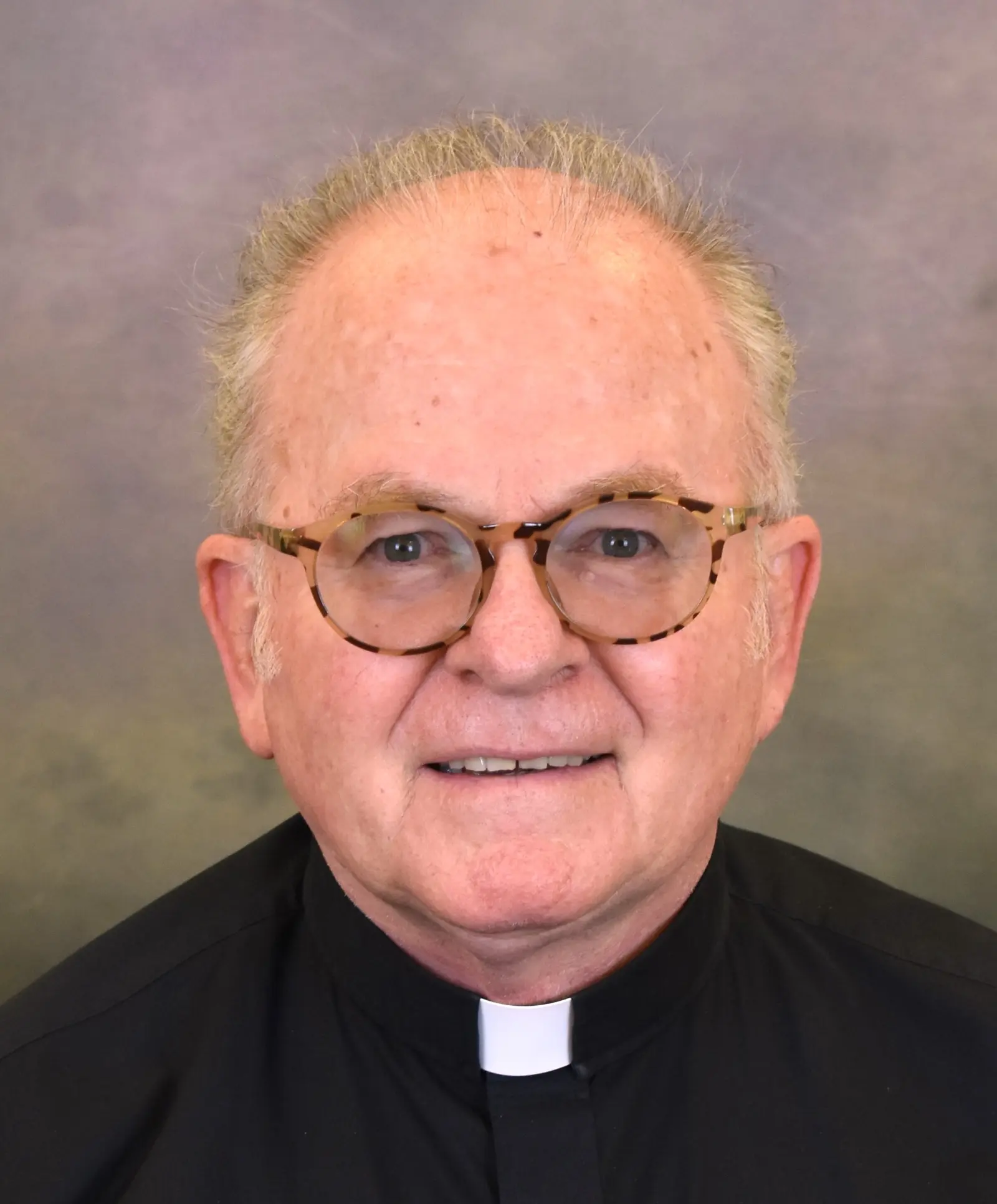 A portrait of a clergyman wearing glasses and a clerical collar.