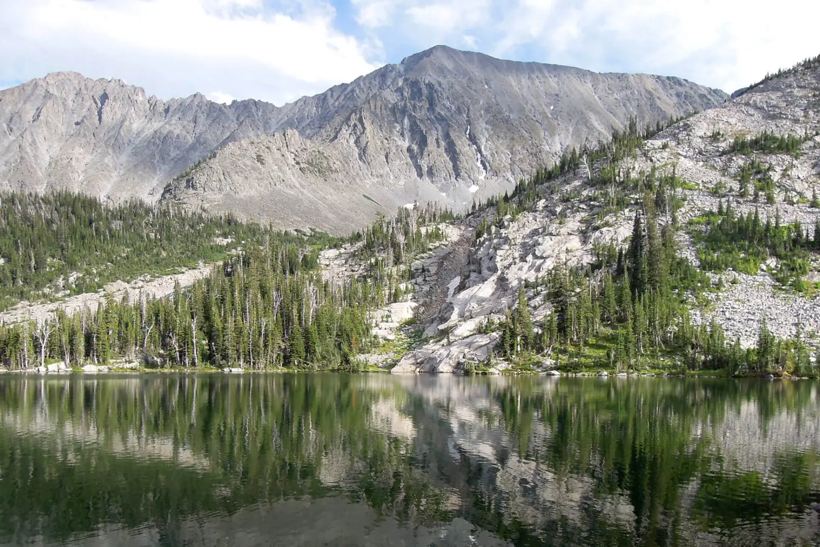 A scenic mountain lake reflects the surrounding peaks and evergreen trees.