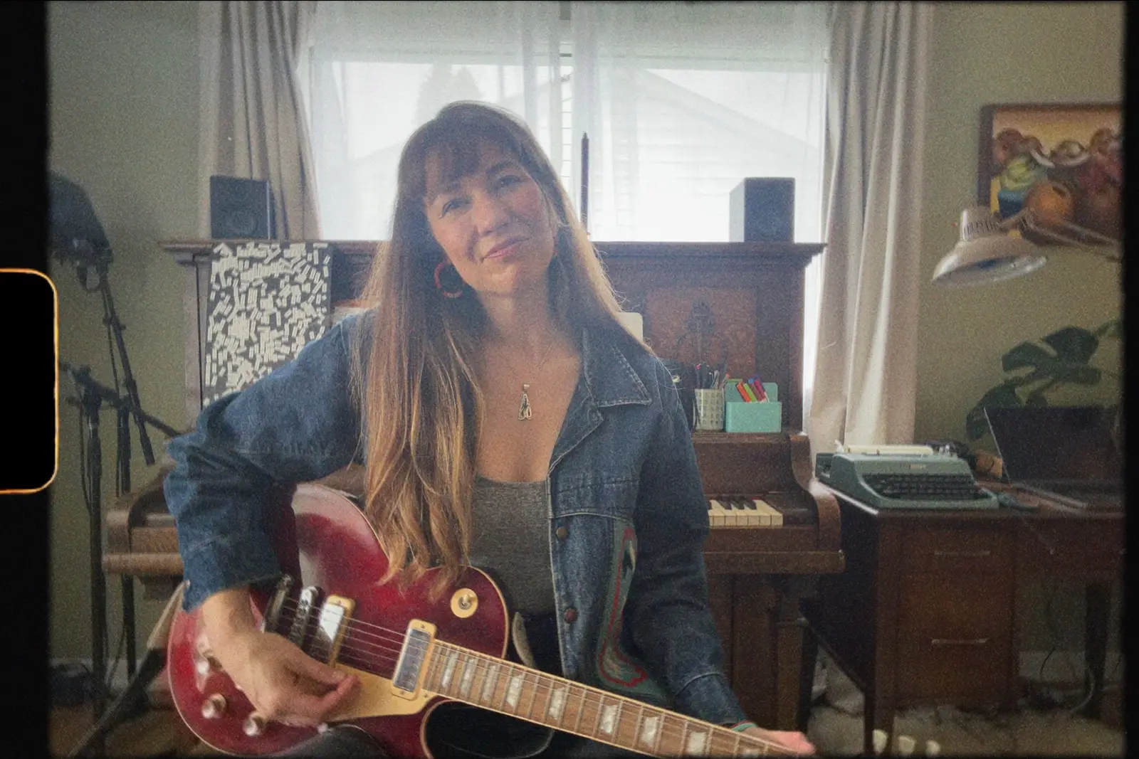 A woman with long brown hair plays a red electric guitar in front of a piano.