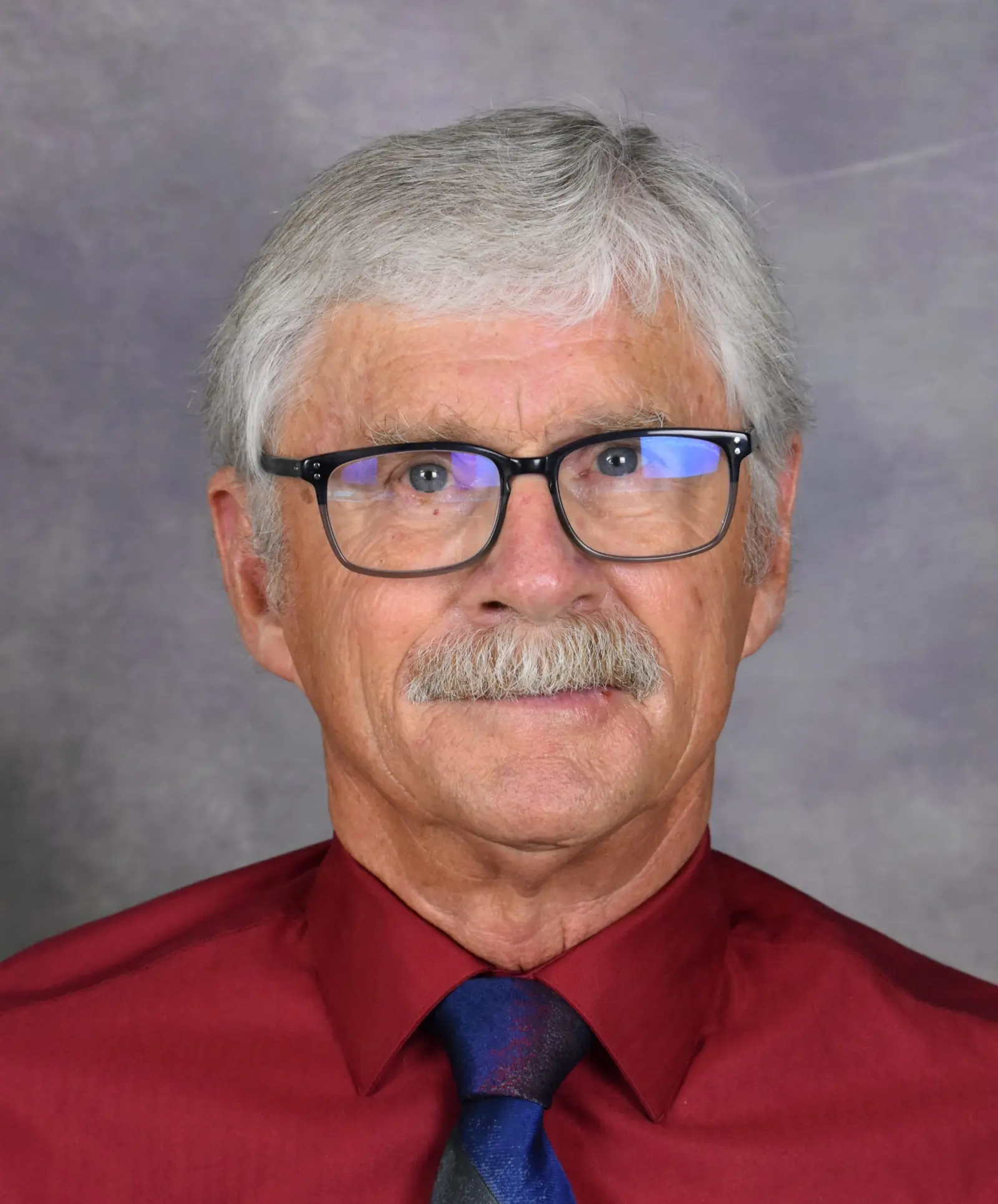 A portrait of an older man with gray hair, glasses, and a mustache wearing a red shirt and tie.