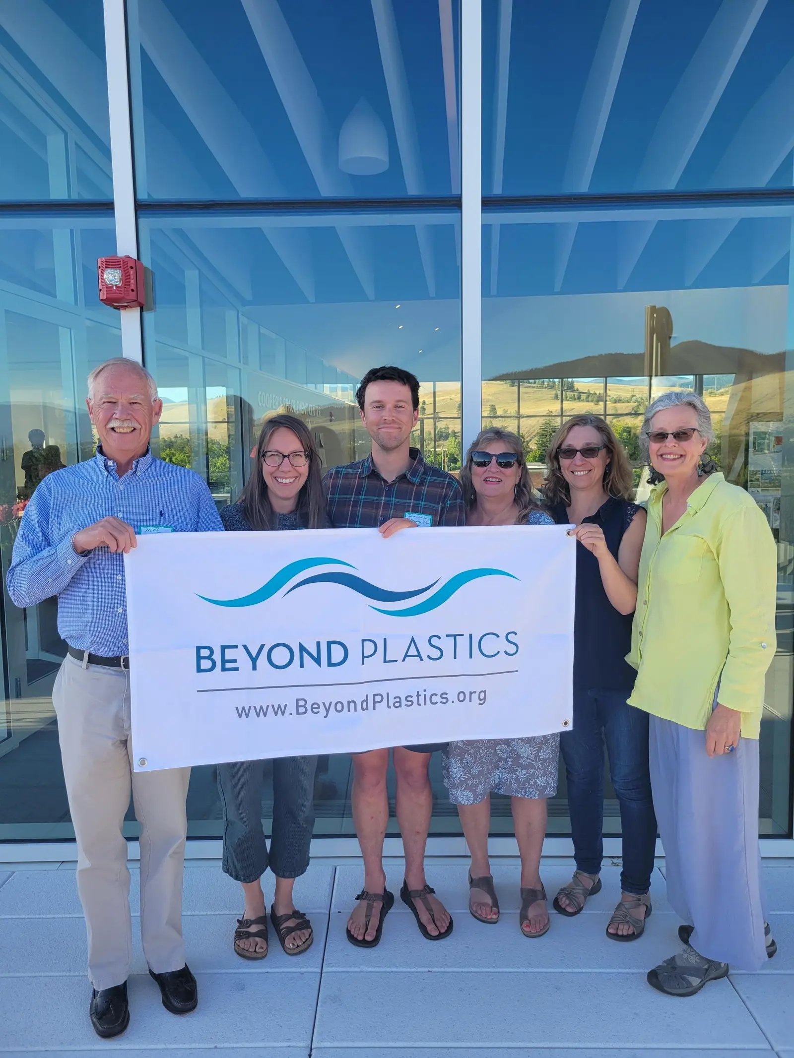 A group of adults stands in front of a building holding a banner for Beyond Plastics.