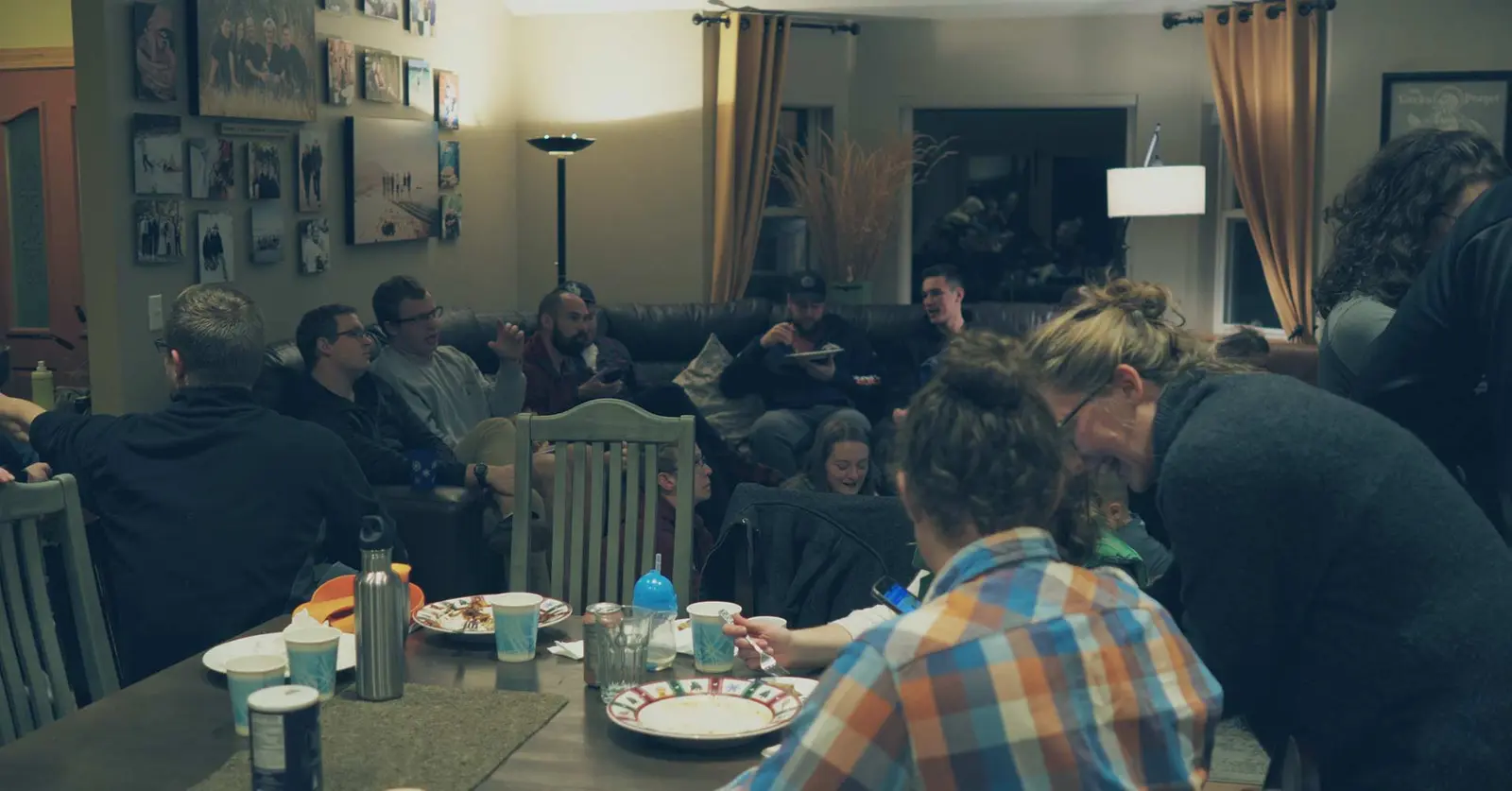 A group of people are socializing in a living room and dining area during a gathering.
