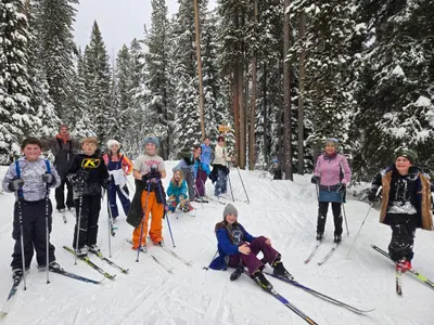 Photo from echolaketrails.org A group of people of various ages wearing winter clothing are cross-country skiing in a snowy forest.