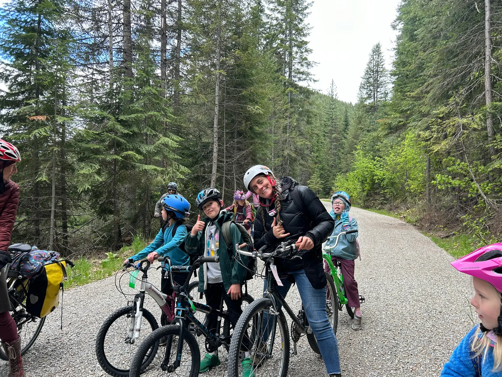 A group of children and an instructor are posing on a dirt path while riding bicycles in a forest.