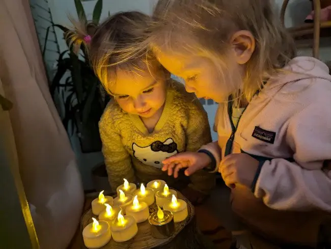 Two children look down at a collection of small lit candles.