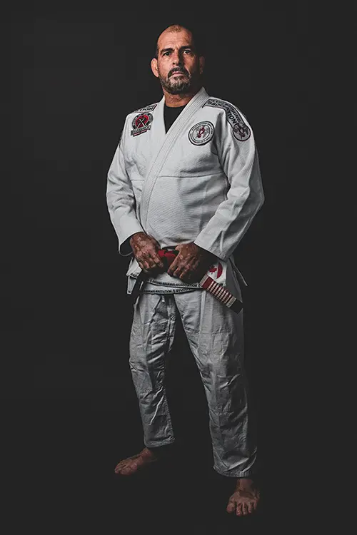 A man wearing a white martial arts uniform stands against a black background.