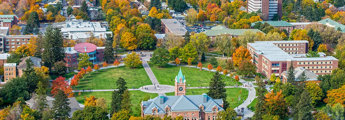 An aerial view of a university campus featuring a large clock tower building surrounded by autumn trees and walkways.