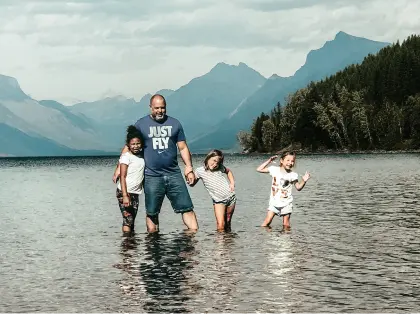 An adoptive father standing with his smiling children in a mountain lake.