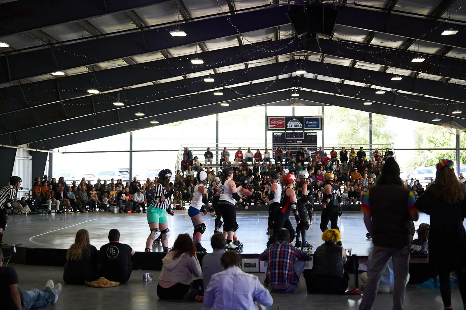 People watch a roller derby match taking place in an indoor arena.
