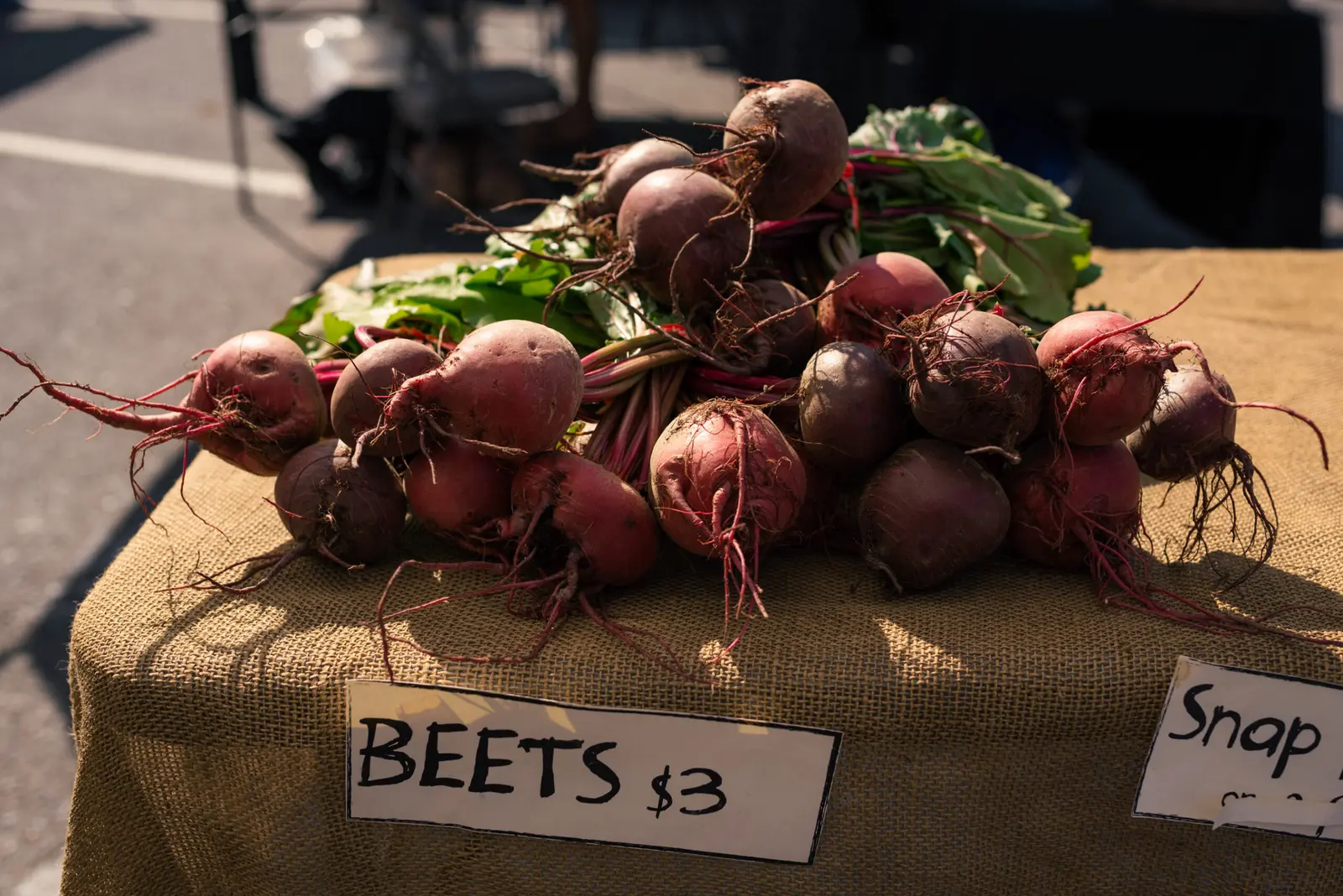 A pile of fresh beets sits on a burlap-covered table at an outdoor market.