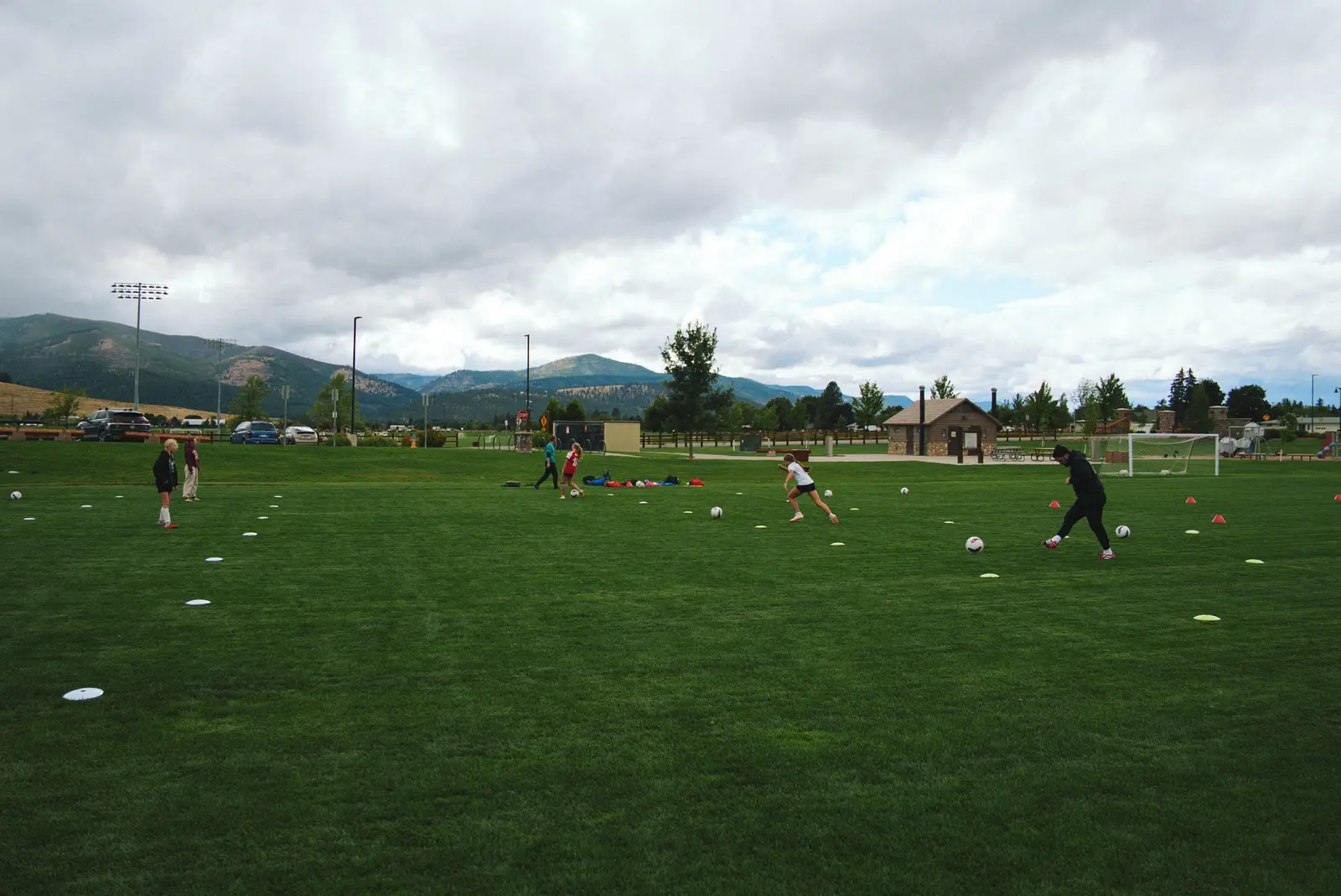 A group of people participate in a soccer training session on a grassy field with mountains in the background.