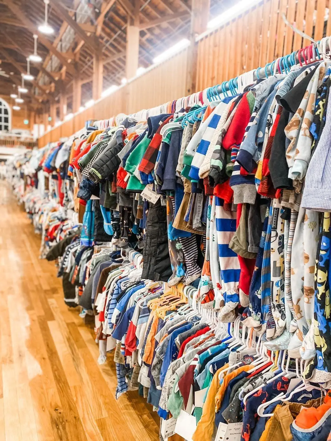 Clothing racks filled with various children's clothes in a store with wooden flooring and ceiling.