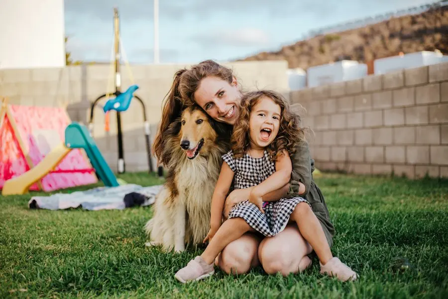 A woman and a young girl sit with their dog on the grass in a backyard.