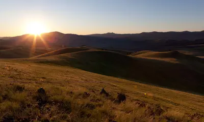 The sun sets over a landscape of grassy rolling hills.