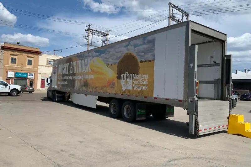A semi-truck with a trailer decorated with branding for a food bank sits in an outdoor parking area.