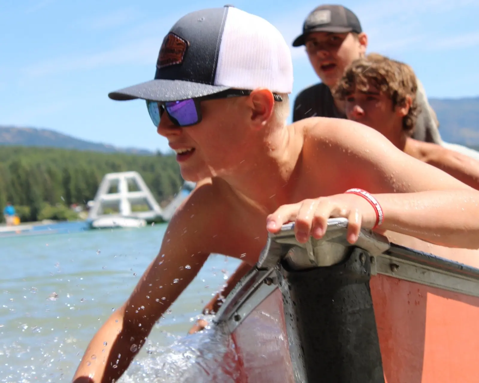 A young man wears a baseball cap and sunglasses while playing in a lake near a boat.