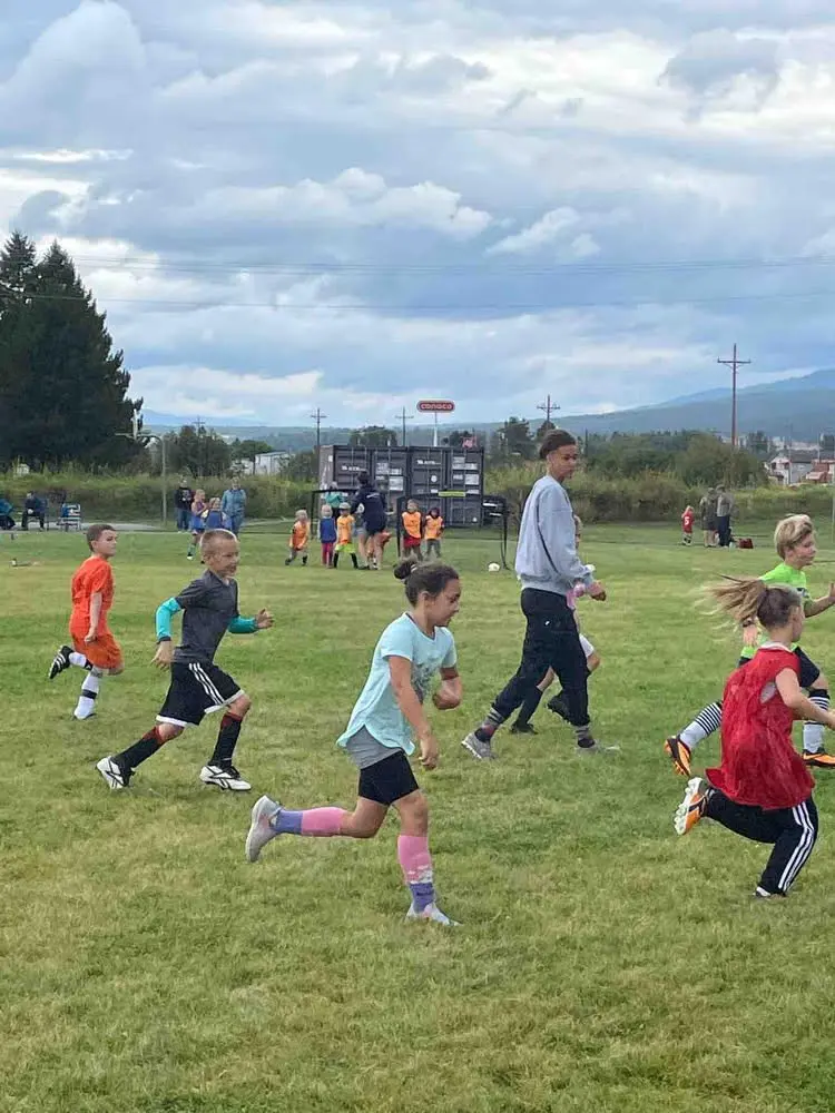A group of children are actively running on a grass field during a sports practice or game.