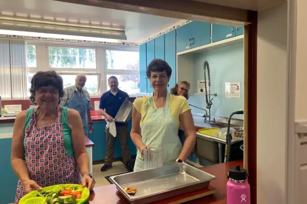 A group of adults wears aprons and prepares food in a kitchen.