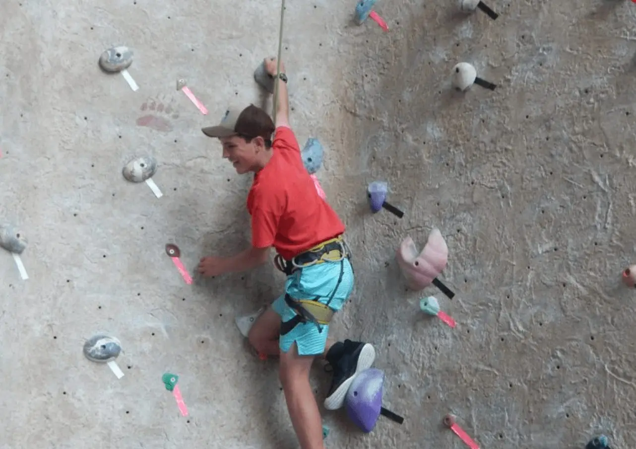 A young boy climbs a rock wall while wearing a harness and safety rope.