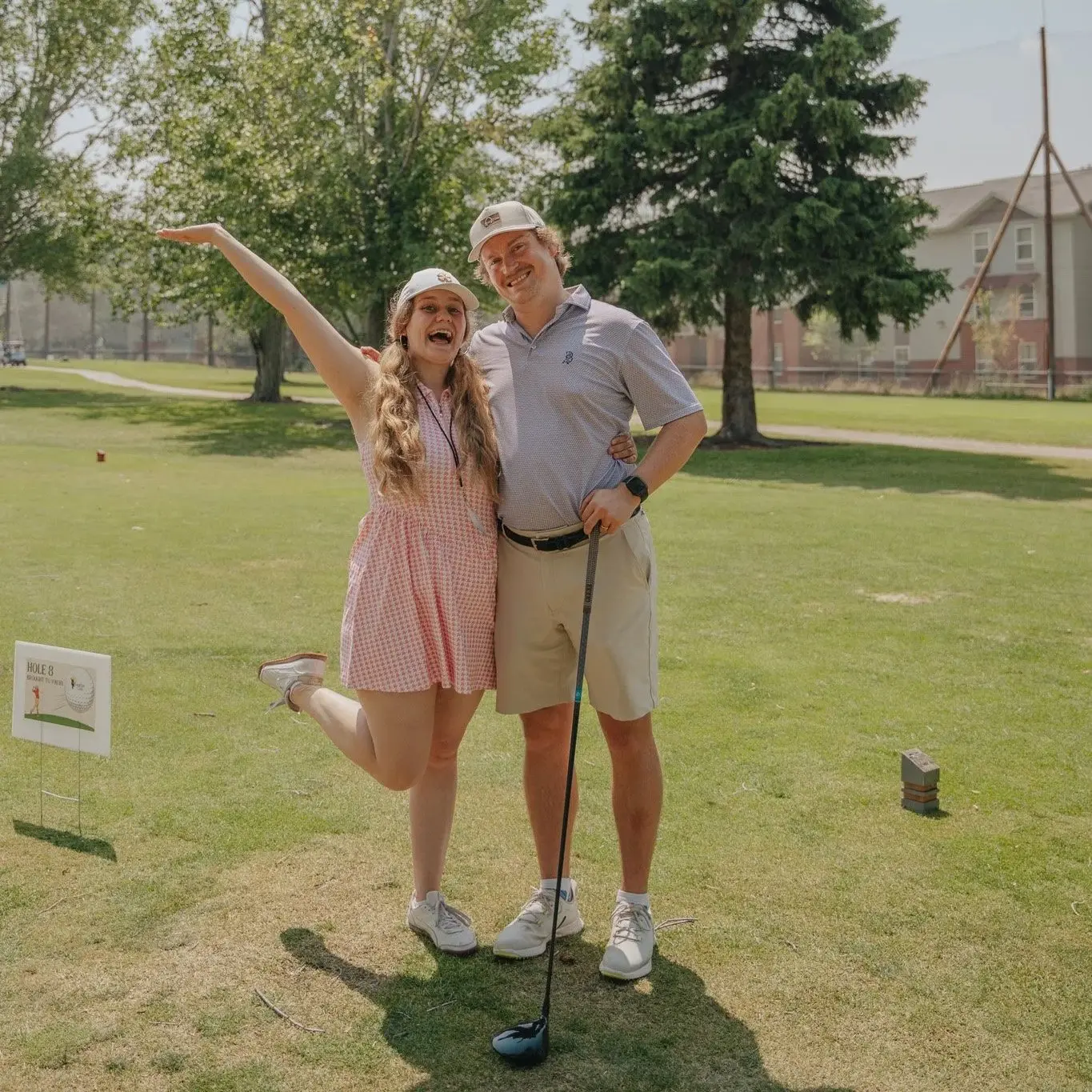 A young man and woman smile together on a golf course.