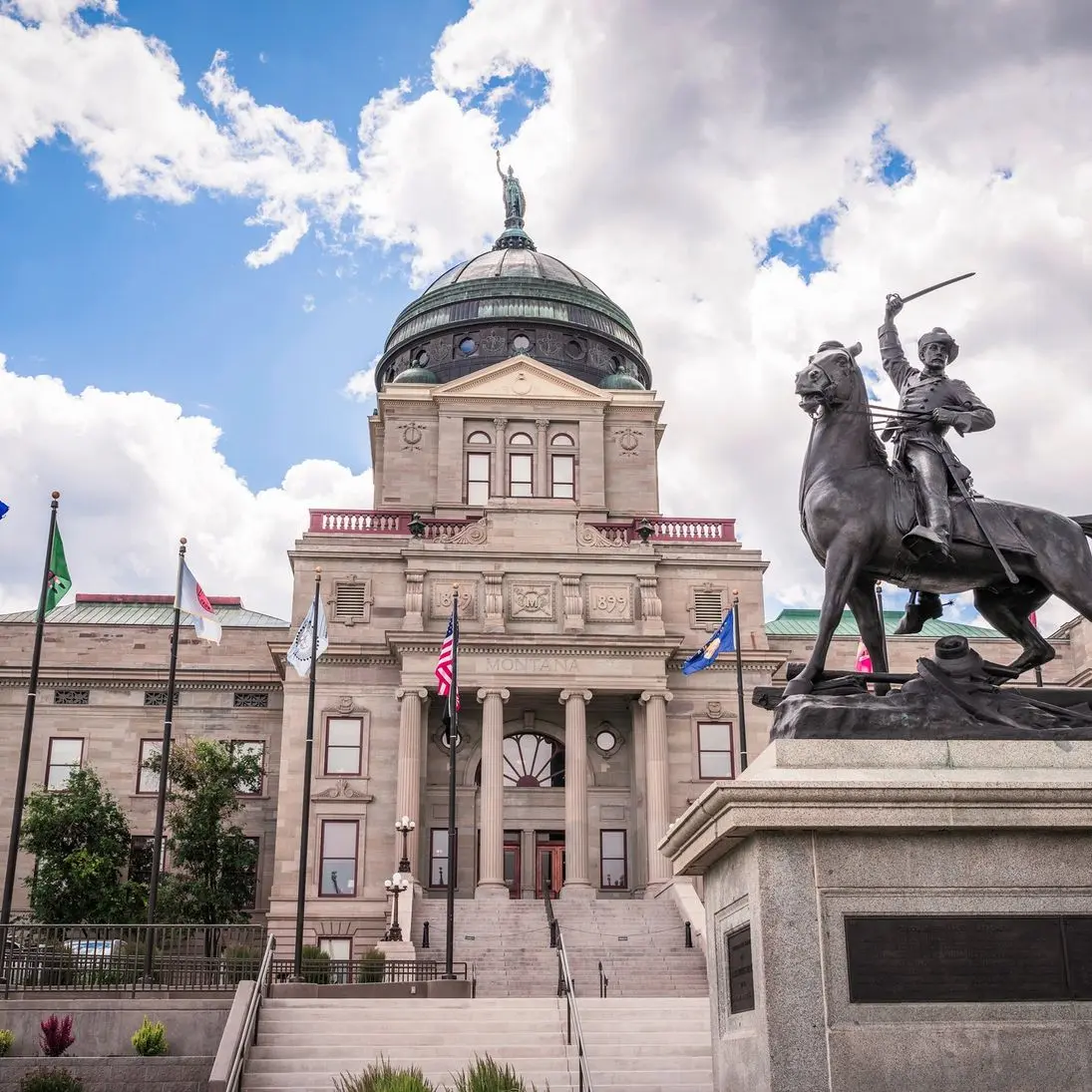 Statue of a soldier on horseback in front of Montana's capitol building under a partly cloudy sky.