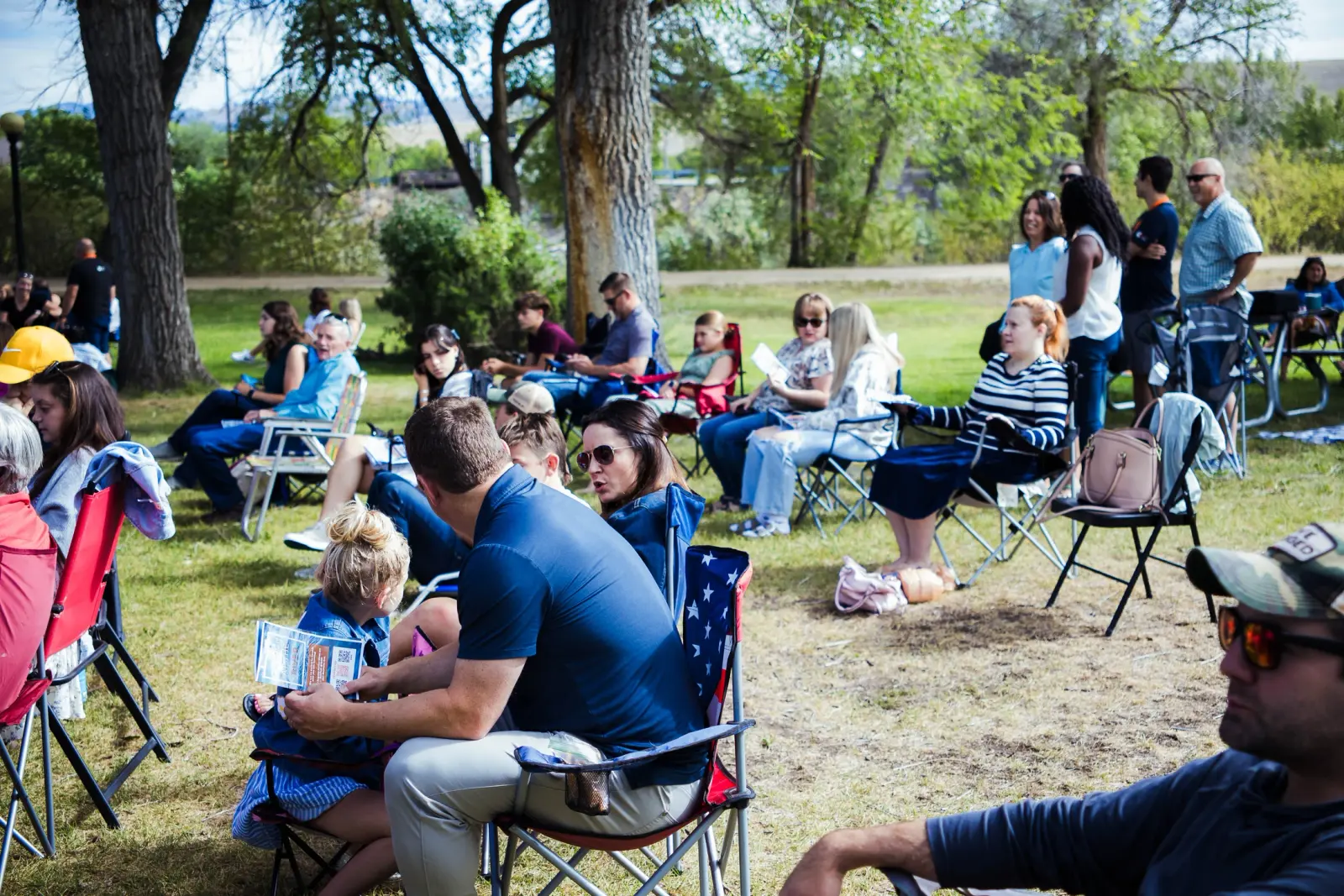 A group of people sitting on chairs in a park area.