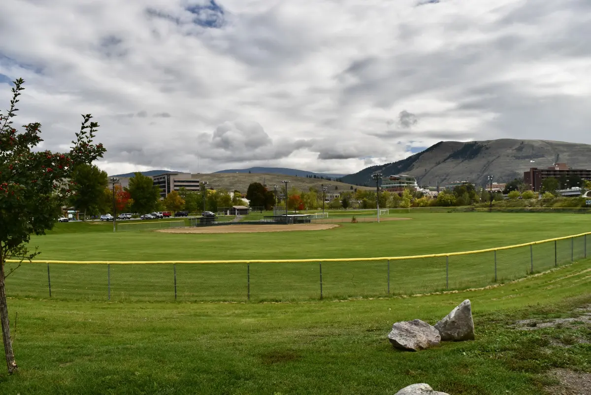 A wide view of a grassy field with a perimeter fence under a cloudy sky.