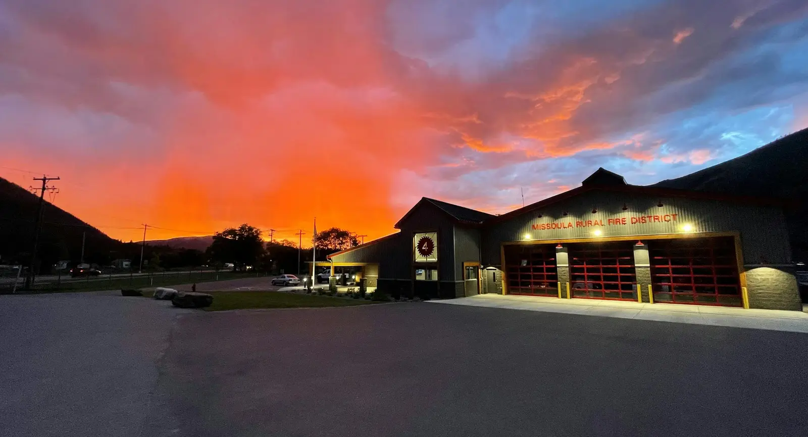 A fire station is shown at sunset with a vibrant orange and purple sky.