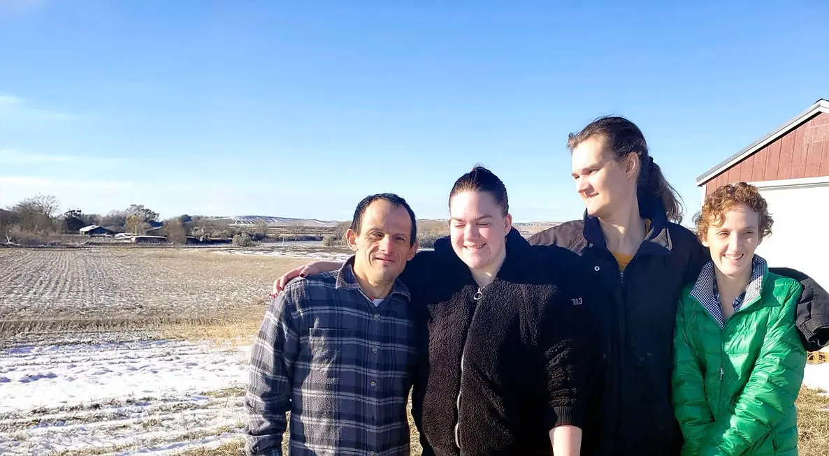 Four people pose for a photo outdoors in a field with light snow on the ground.