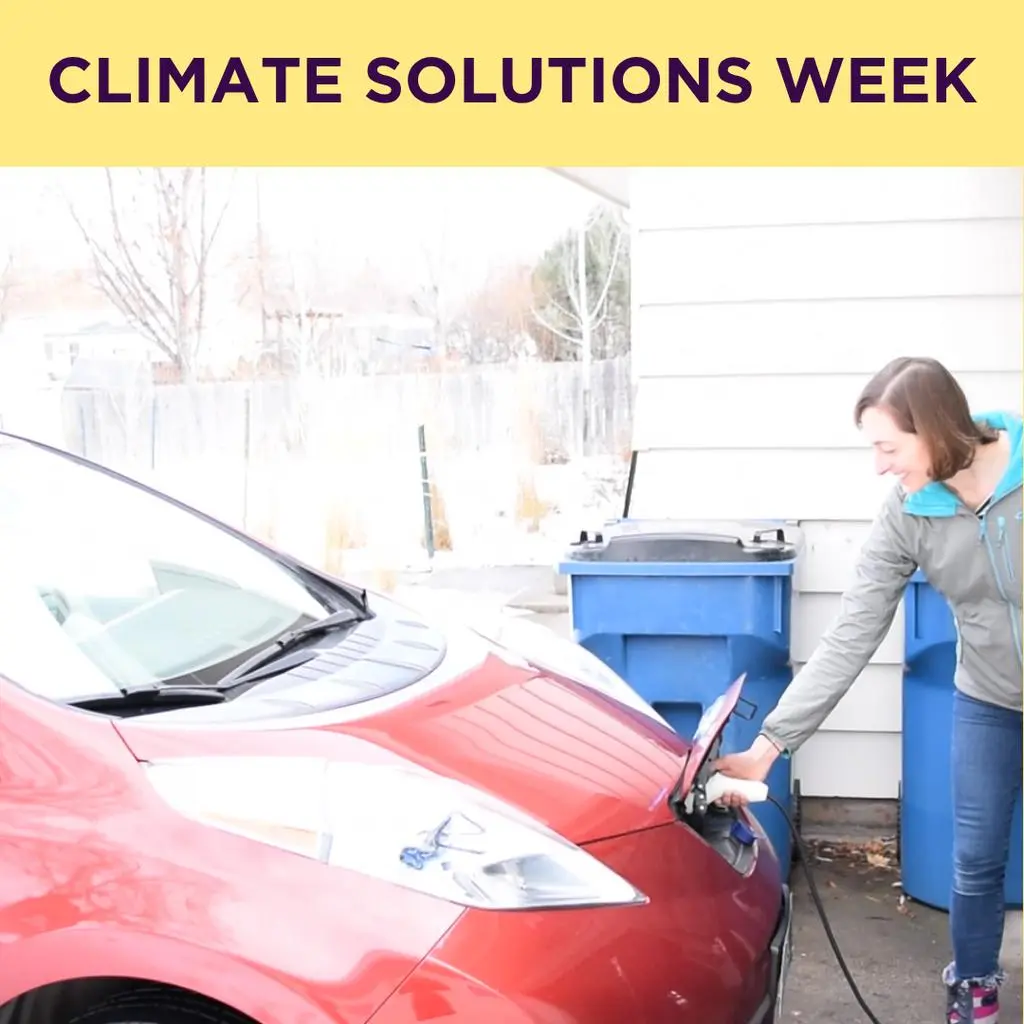A woman plugs a charging cable into an electric vehicle next to blue bins with the text "Climate Solutions Week" at the top.