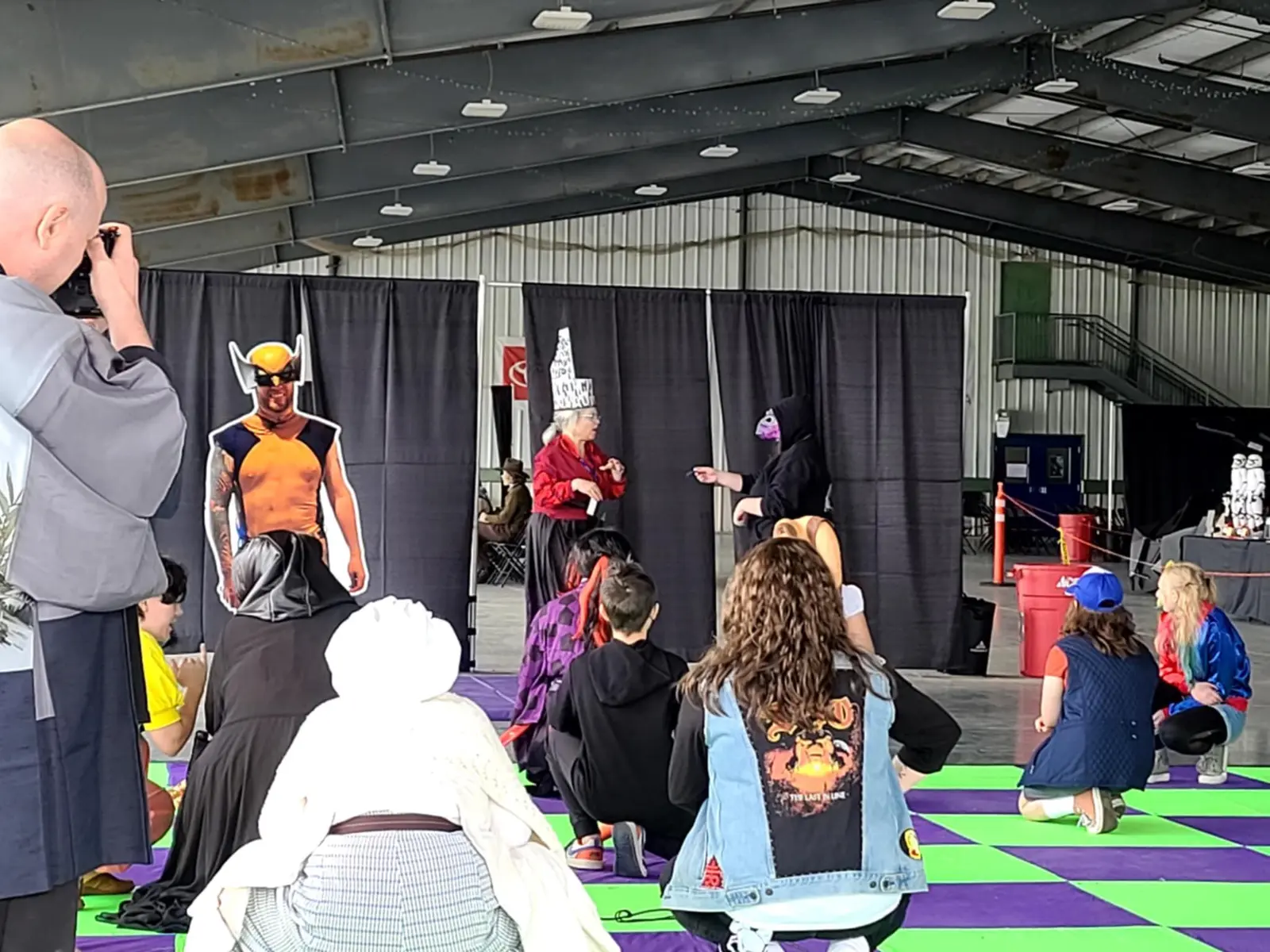 People watch individuals in costumes at an indoor event.
