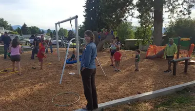 Photo from flickr.com A woman stands in the foreground at a playground where children are playing.