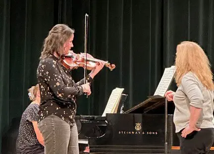 A person plays the violin during a musical performance while another person watches.