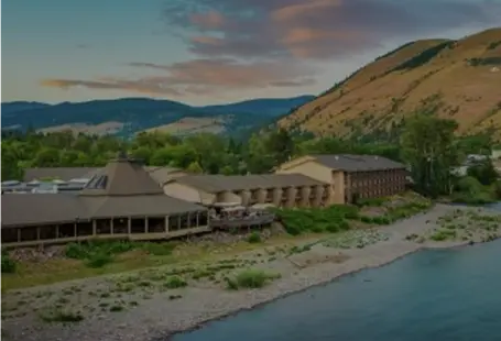 A hotel building sits alongside a river in a mountainous landscape.